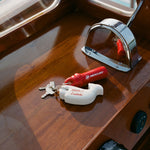 Close-up of boat dashboard with a whale-shaped white key float labeled 'Boston Whaler' and 'Tombolo' attached to a keyring. Also attached is a red Mercury engine kill switch.