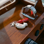 Set of boat keys with a red Mercury float and white Tombolo-branded whale keychain resting on a wooden boat console.