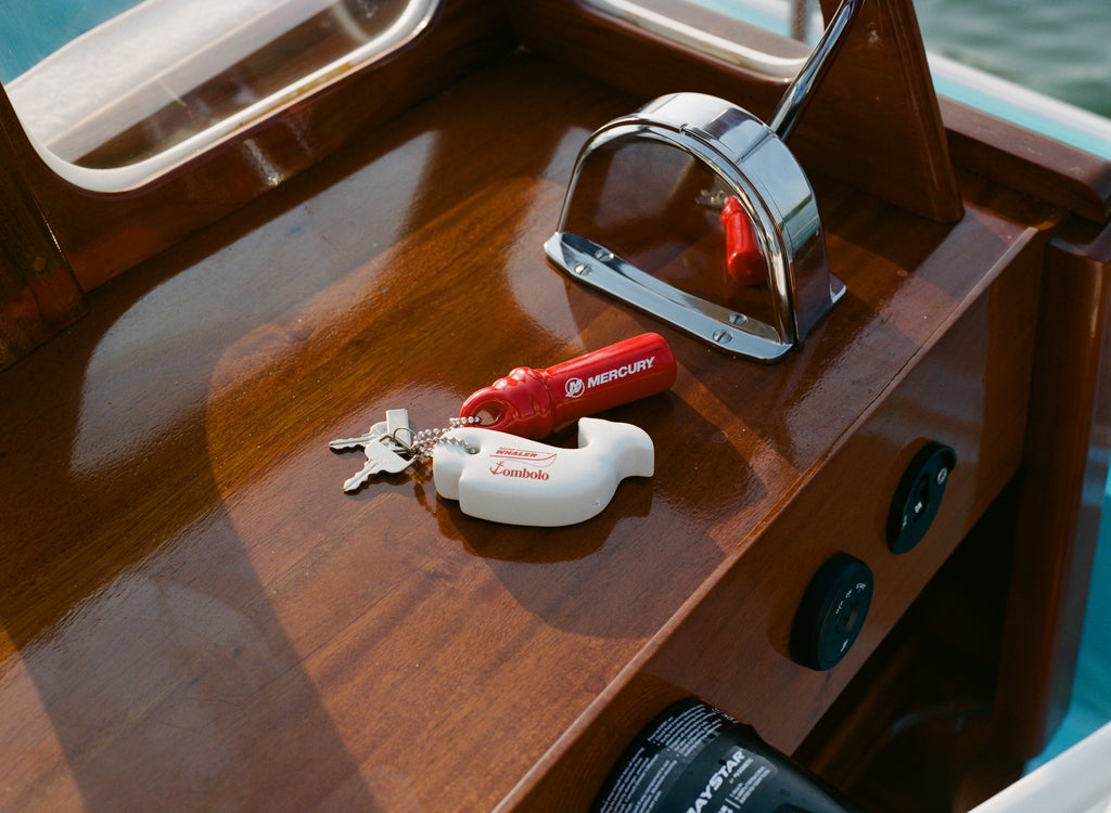 Set of boat keys with a red Mercury float and white Tombolo-branded whale keychain resting on a wooden boat console.