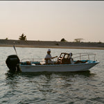 Small boat with a motor on a body of water during sunset.