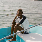 Woman sitting on a boat wearing a light blue cotton mesh shirt with navy shoulder panels and a 'Boston Whaler' logo on the chest, paired with matching navy shorts with white trim. 