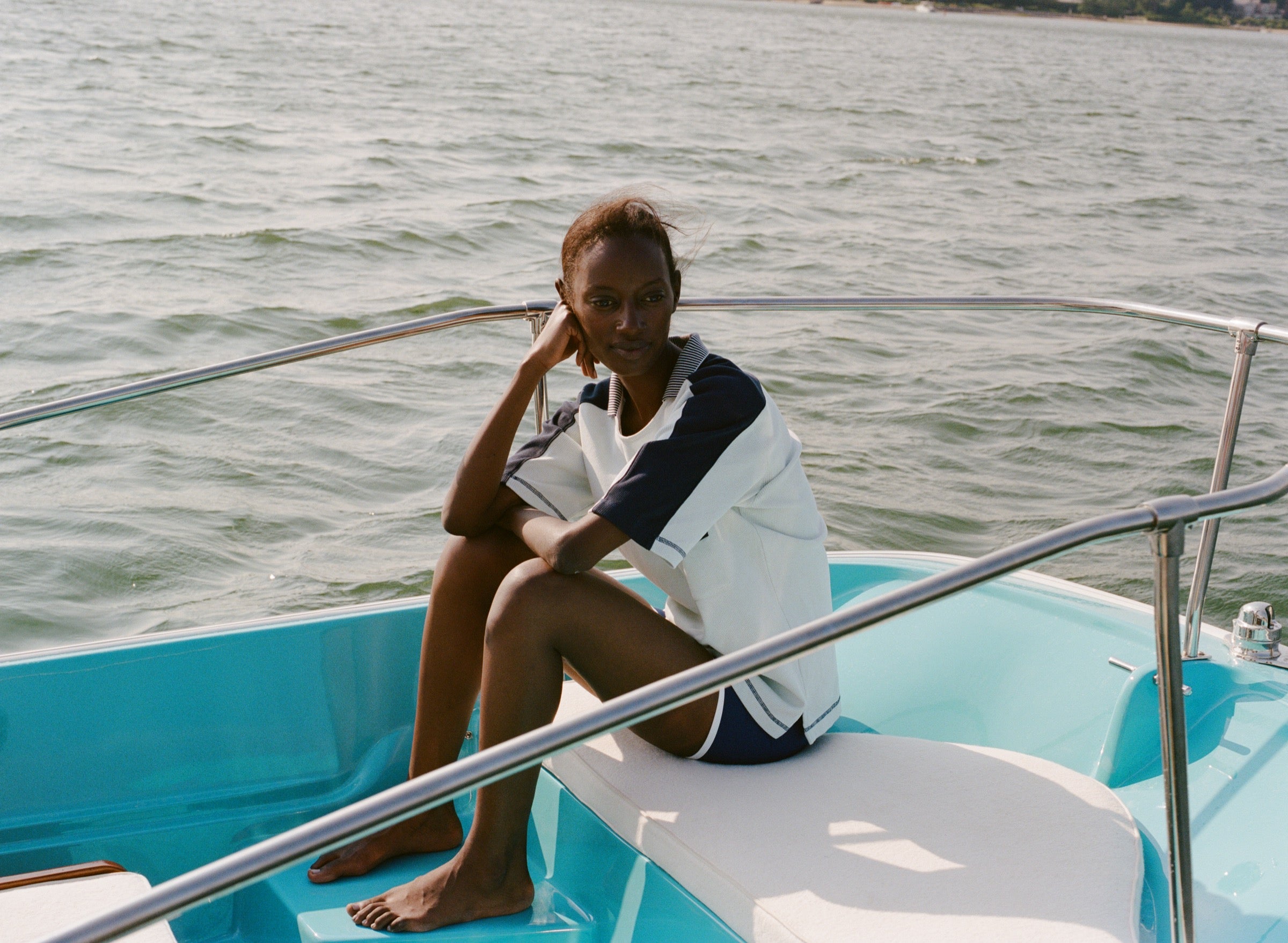 Woman sitting on a boat wearing a light blue cotton mesh shirt with navy shoulder panels and a 'Boston Whaler' logo on the chest, paired with matching navy shorts with white trim. 