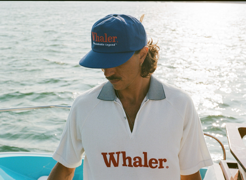 Man on a boat wearing a blue 'Whaler' hat and a white collared shirt with 'Whaler' printed on it.