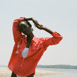Woman standing on the beach, wearing a red button-up shirt over a white one-piece swimsuit. 