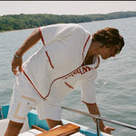 Man leaning over side of boat while wearing the white hooded zip-up beach towel top with red trim and vertical 'Whaler' text.