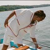 Man leaning over side of boat while wearing the white hooded zip-up beach towel top with red trim and vertical 'Whaler' text.