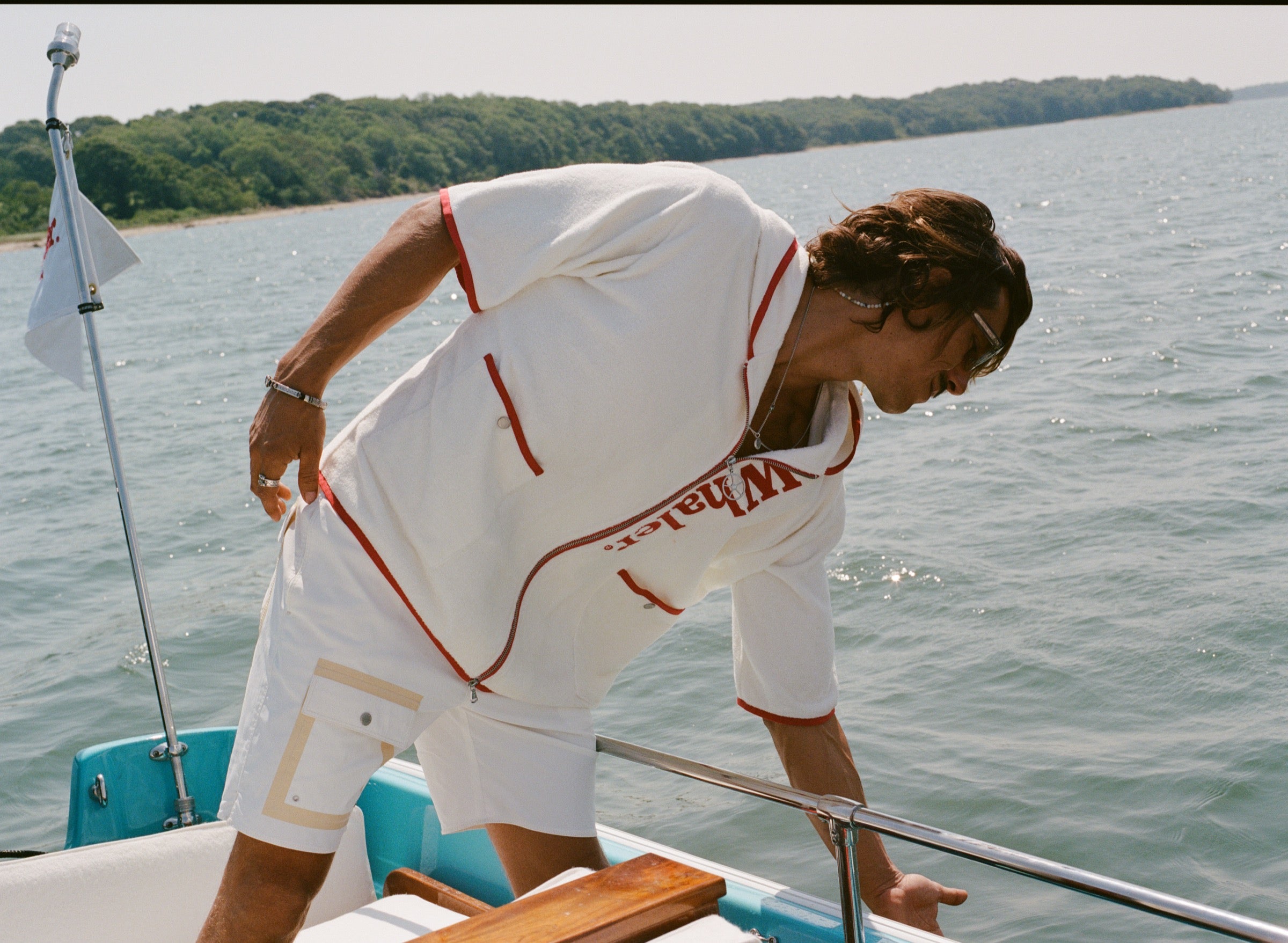 Man leaning over side of boat while wearing the white hooded zip-up beach towel top with red trim and vertical 'Whaler' text.