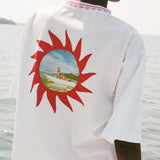 ChatGPT said:
Back of a white t-shirt with chain-stitched sunburst artwork framing a printed vintage photo of someone standing on a boat.