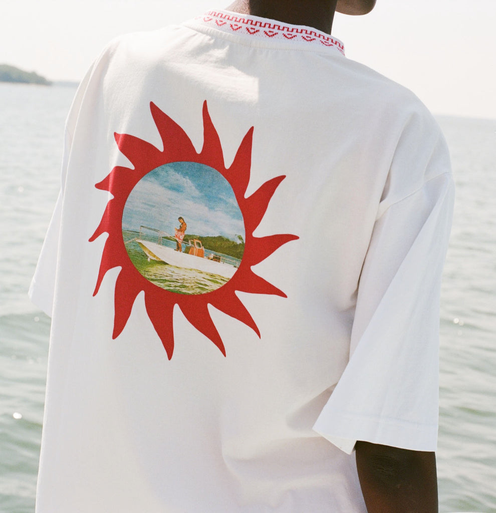 ChatGPT said:
Back of a white t-shirt with chain-stitched sunburst artwork framing a printed vintage photo of someone standing on a boat.