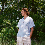 Man stands in grass wearing a light blue zip-up shirt with four front pockets, each fastened with red or green buttons, and khaki shorts with the word 'Whaler' embroidered on the pocket.