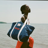 Woman standing in the sun, holding the navy 'Whaler' canvas tote bag with white handles over her shoulder.