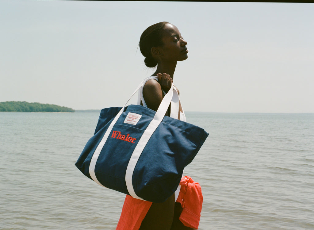 Woman standing in the sun, holding the navy 'Whaler' canvas tote bag with white handles over her shoulder.
