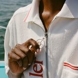 Close-up of woman wearing the white terry short-sleeve zip up with red contrast stitching, zipping up the shirt with the silver ship wheel zipper pull.