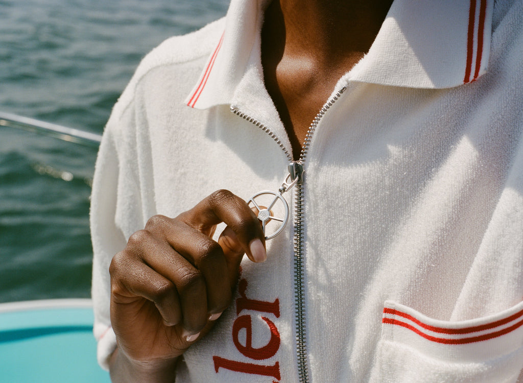 Close-up of woman wearing the white terry short-sleeve zip up with red contrast stitching, zipping up the shirt with the silver ship wheel zipper pull.