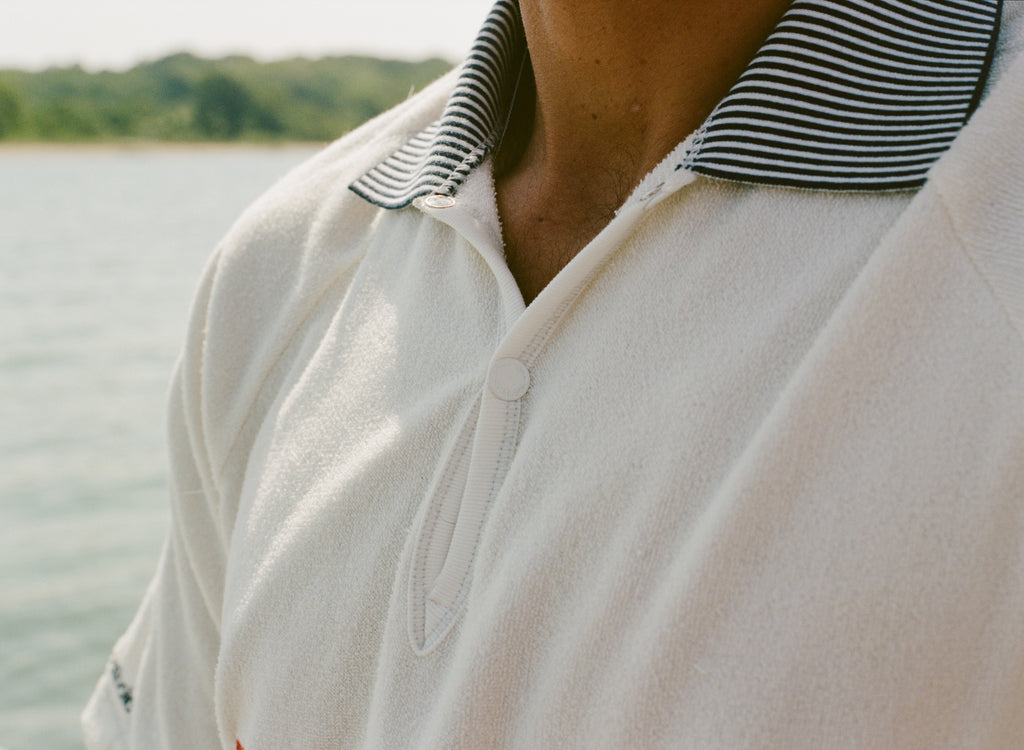Close-up of a white terry polo shirt with a black-and-white striped collar and a single snap button on the placket. 