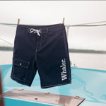 Navy board shorts with white contrast stitching hanging on a clothing rod with clothespins.