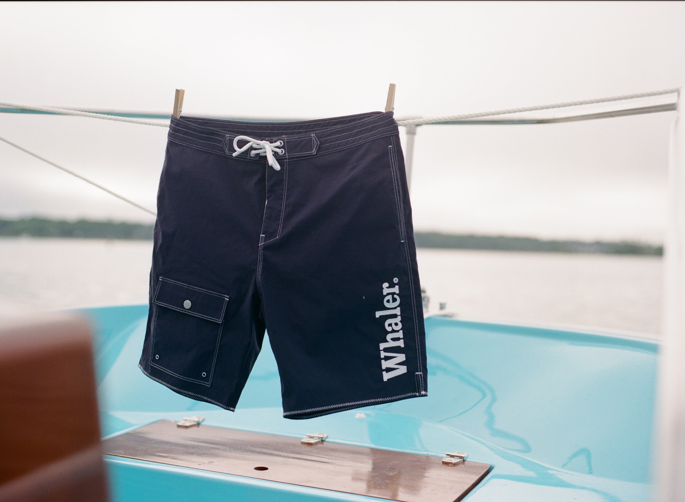 Navy board shorts with white contrast stitching hanging on a clothing rod with clothespins.