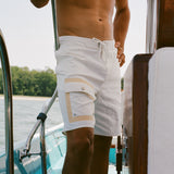 Close-up of a man wearing white board shorts with beige-trimmed cargo pockets and a drawstring waist, standing on a boat.