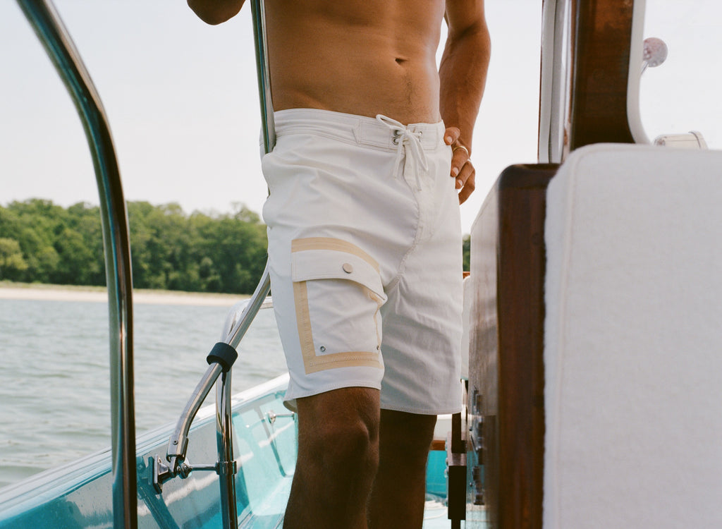 Close-up of a man wearing white board shorts with beige-trimmed cargo pockets and a drawstring waist, standing on a boat.