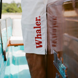Close-up of white board shorts with bold red 'Whaler' text printed vertically on the left leg.