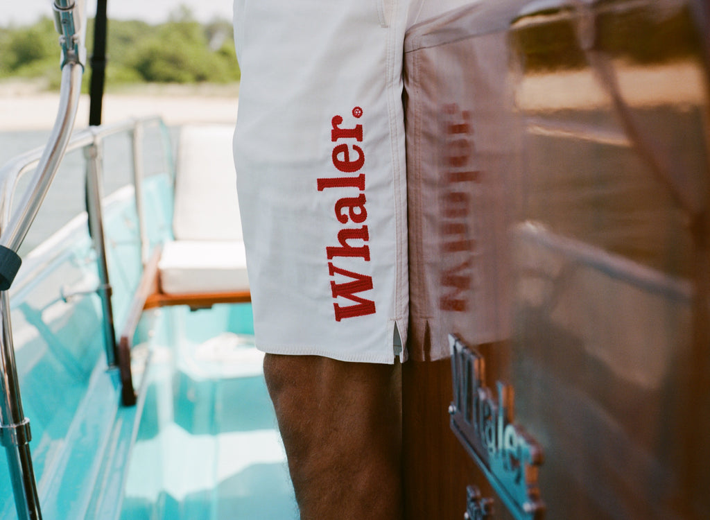 Close-up of white board shorts with bold red 'Whaler' text printed vertically on the left leg.