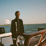 Woman wearing a 'Whaler' Cardigan while standing at the wheel on a boat on water. 