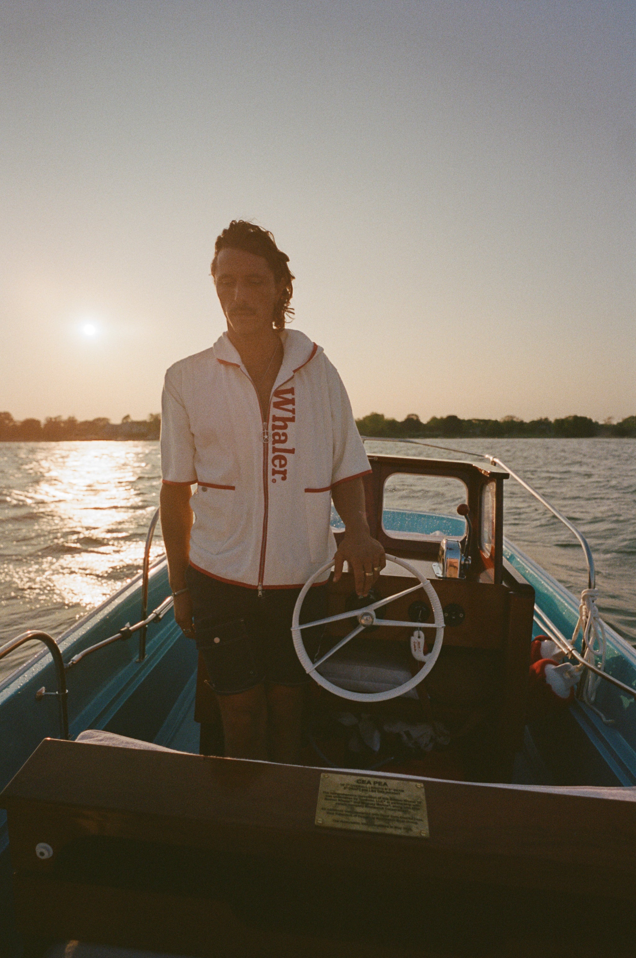 Man on boat wearing the 'Boston Whaler' 1961 Cabana, standing at the wheel.