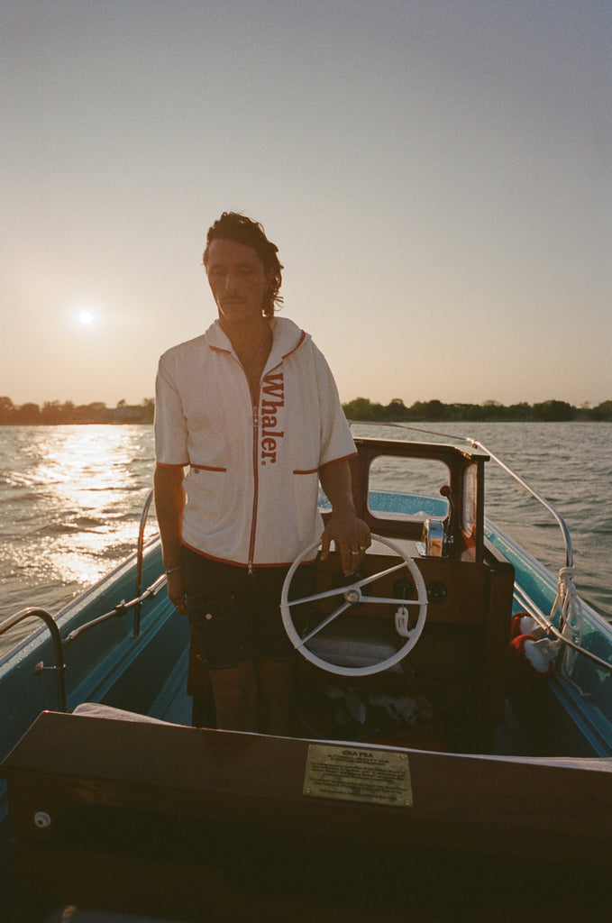 Man on boat wearing the 'Boston Whaler' 1961 Cabana, standing at the wheel.