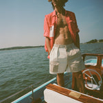 Man on a boat wearing two-tone khaki and off-white shorts with a side flap pocket and a red fishing shirt with a white mesh pocket.