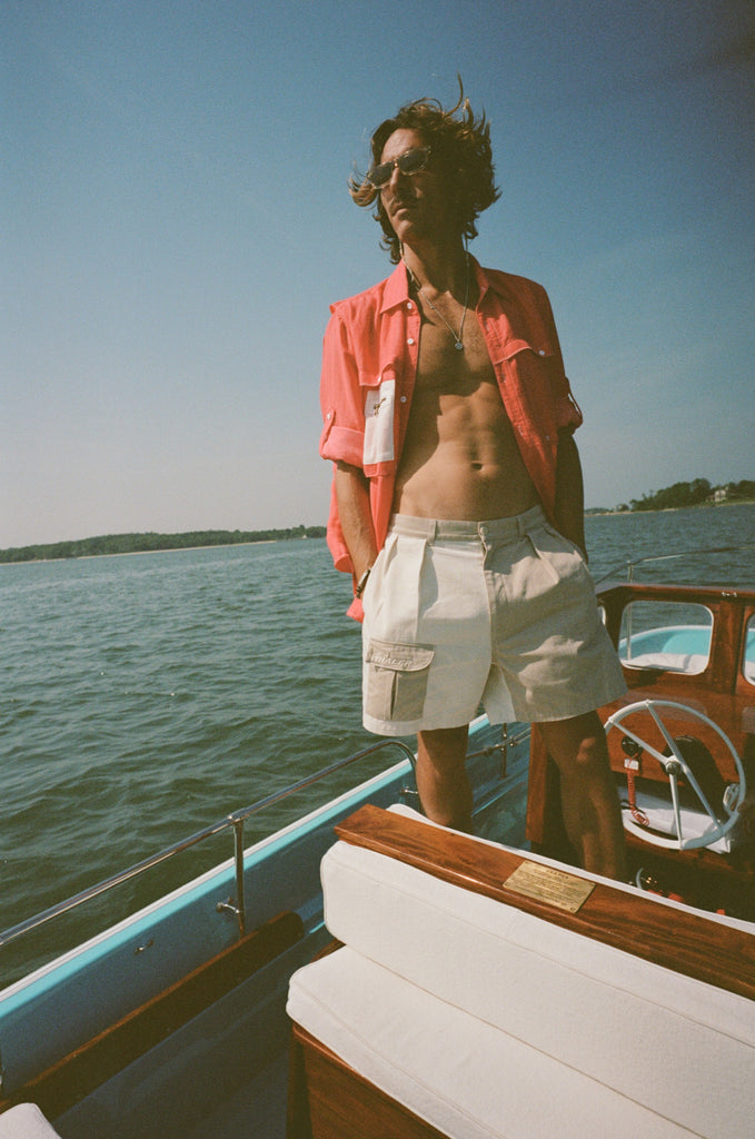 Man on a boat wearing two-tone khaki and off-white shorts with a side flap pocket and a red fishing shirt with a white mesh pocket.