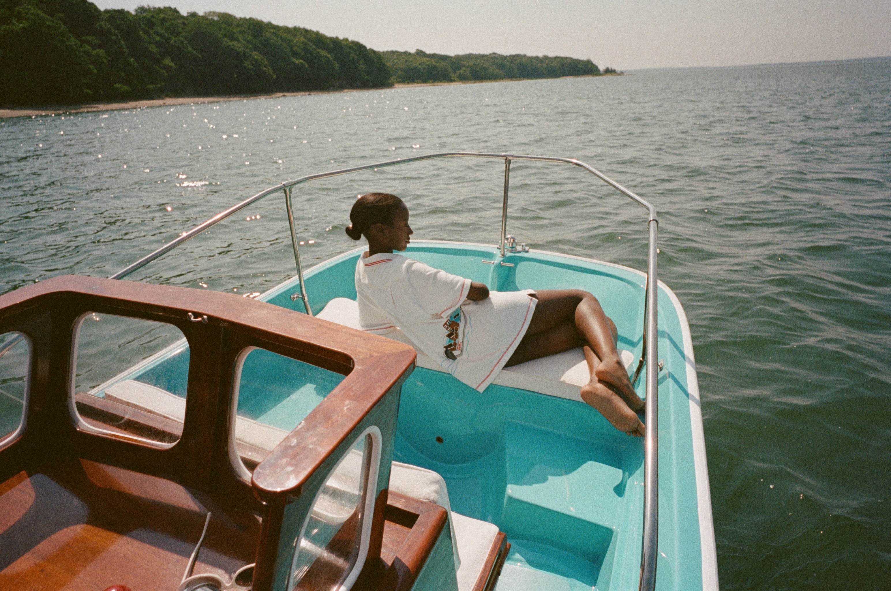 Woman lying on a boat, wearing the white terry 'Boston Whaler' Cabana with a boat embroidery on the back. Her back is to the camera.