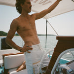 Shirtless man standing on a boat wearing white board shorts with a beige utility pocket and lace-up waist.