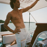 Shirtless man standing on a boat wearing white board shorts with a beige utility pocket and lace-up waist.