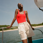 Woman standing on a boat wearing two-tone khaki and off-white "Boston Whaler' shorts with a red one-piece swimsuit underneath. 