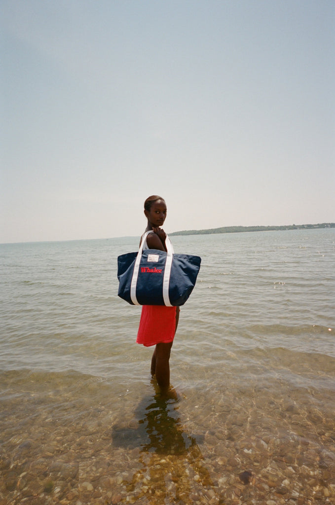 Woman standing in shallow water, holding the Navy canvas tote bag with white handles over her shoulder.