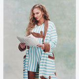 Female model holding a newspaper with long blonde hair wearing 'The Sopranos' Fowl Play Robe alongside matching Fowl Play of shorts and shirt.