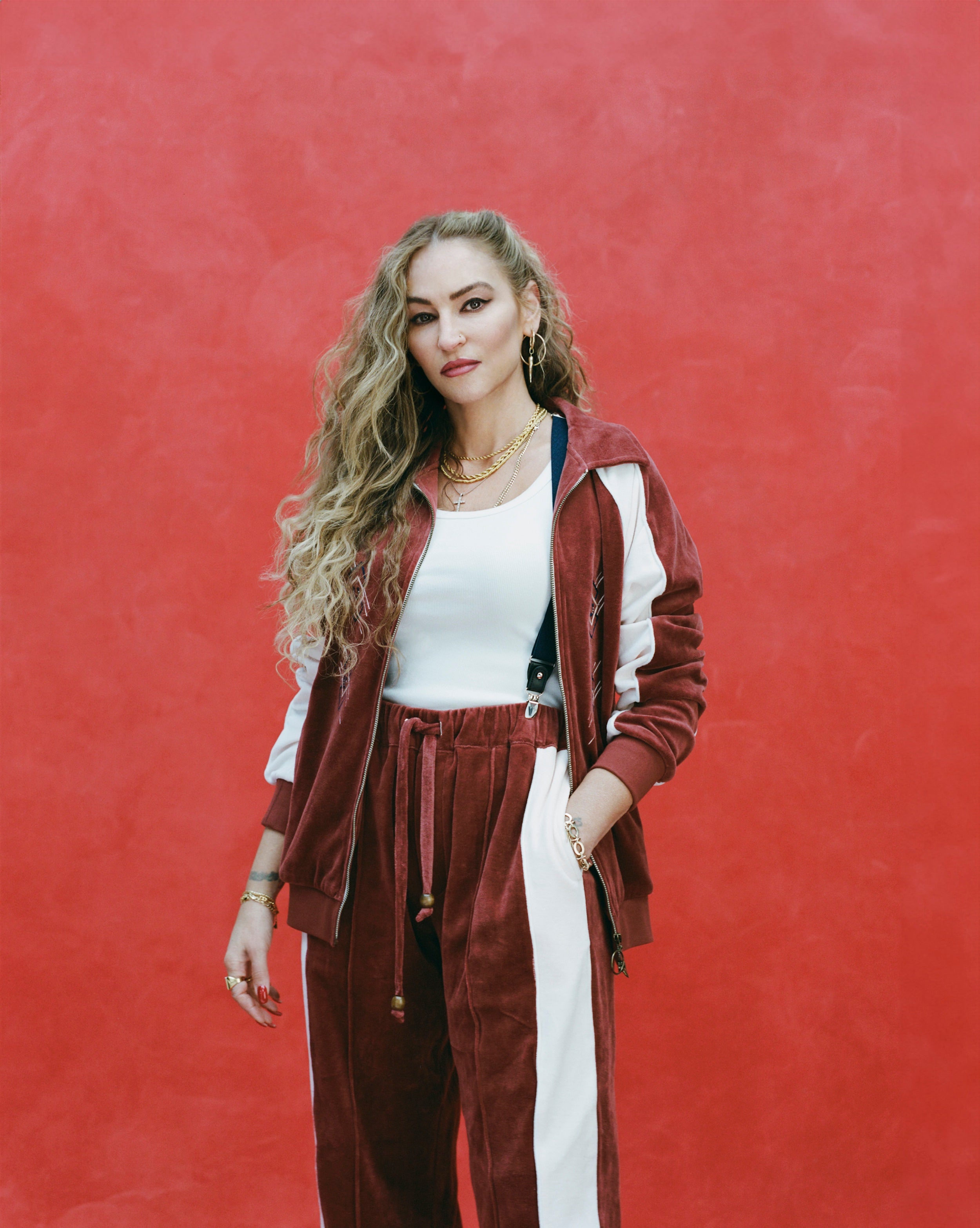 Female model with long blonde hair wearing 'The Sopranos' Pie-O-My Track Pants with a white shirt and a matching Pie-O-My Jacket, shot a textured red background.