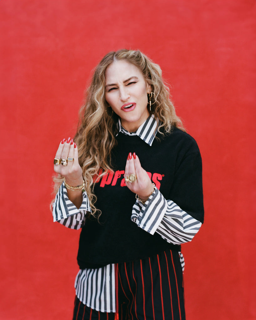 Female model with long blonde hair wearing 'The Sopranos' Souvenir Terry tee over a black-striped collared shirt, alongside navy and red-striped pants.