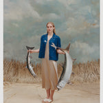 Female model with long blonde hair wearing an unbuttoned 'Teamwork' Cabana ~ Crop Cut with a full-length gold-colored silk dress and white sandals while holding two replica model fish against a light blue and white textured background with waist high beige grass.