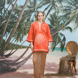 Female model with long blonde hair wearing the 'Scallop' Beach Towel Top and a mesh full-length skirt in khaki coloring with white sandals, shot on a background of a sunny beach with palm trees and a bamboo chair.