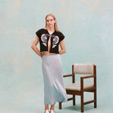 Female model with long blonde hair wearing the 'fish smooch' hand towel top with a light blue silk dress and white sandals, shot on a light blue textured background.