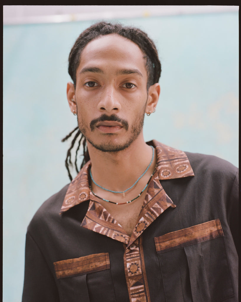 Close up image of a young male model wearing 'The Sopranos' Turnpike Batik that showcases its contrasting batik collar, cuffs, placket, and bottom sweep, in addiction to its Double chest pockets with concealed interior buttons.