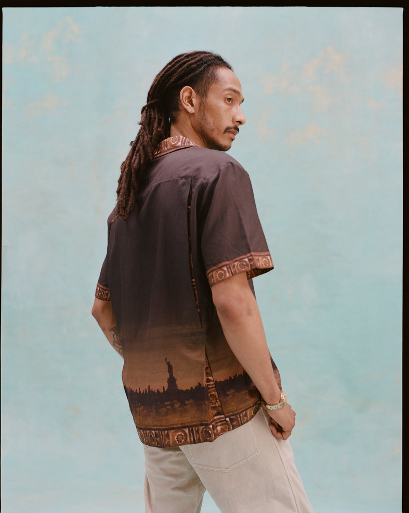 Young male model wearing 'The Sopranos' Turnpike Batik turned slightly away from the camera, looking over his shoulder with the digitally printed skyline of New York City and the Statue of Liberty showing.