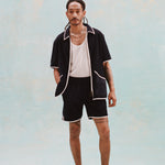 Male model with dreadlocks wearing the 'Standard Issue' Cabana (Midnight Blue) fully unzipped with a white tank top beneath it, matching 'standard issue' shorts in midnight blue, and white slippers, all shot on a white background.