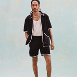 Male model with dreadlocks wearing the 'Standard Issue' Cabana (Midnight Blue) fully unzipped with a white tank top beneath it, matching 'standard issue' shorts in midnight blue, and white slippers, all shot on a white background.