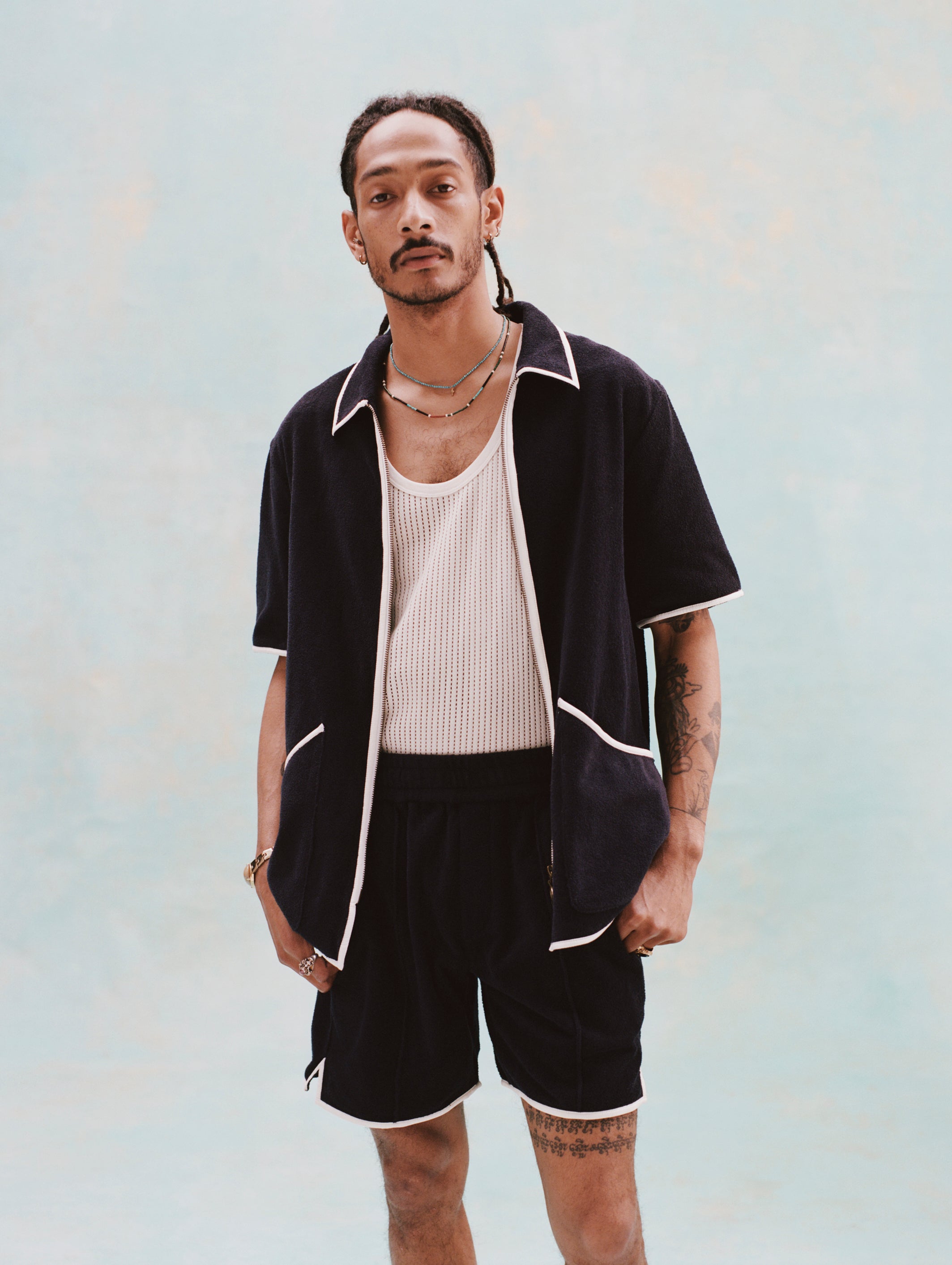 Male model with dreadlocks wearing the 'Standard Issue' Cabana Shorts (Midnight Blue) alongside a matching unzipped 'Standard Issue' Cabana in Midnight blue with a white, mesh tanktop underneath.