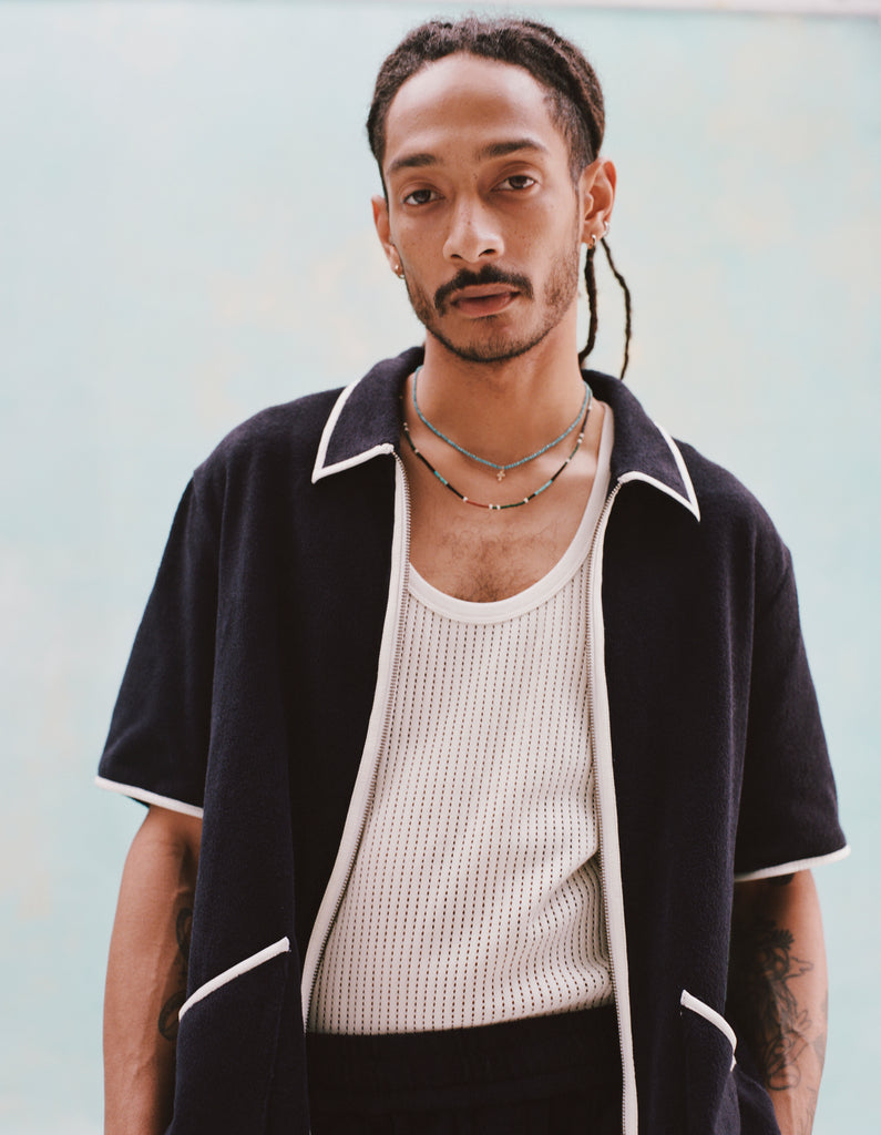 Male model with dreadlocks wearing the 'Standard Issue' Cabana (Midnight Blue) fully unzipped with a white tank top beneath it, and matching 'Standard Issue' Shorts in midnight blue, all shot on a white background.