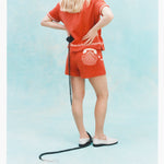 Back view of a woman wearing a matching orange terry cloth shirt and shorts set with white embroidered details, including a telephone and seashell motif on the shorts. 