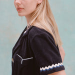 Female model with long blonde hair turned to the side with her face towards the camera wearing the 'Rick Rack' Cabana ~ Crop Cut (Midnight Blue), shot on a textured light blue background.