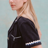 Female model with long blonde hair turned to the side with her face towards the camera wearing the 'Rick Rack' Cabana ~ Crop Cut (Midnight Blue), shot on a textured light blue background.